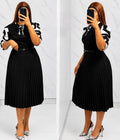 Pleated midi dress featuring puff sleeves, ribbon accents, a defined waistline, and a flowing skirt.