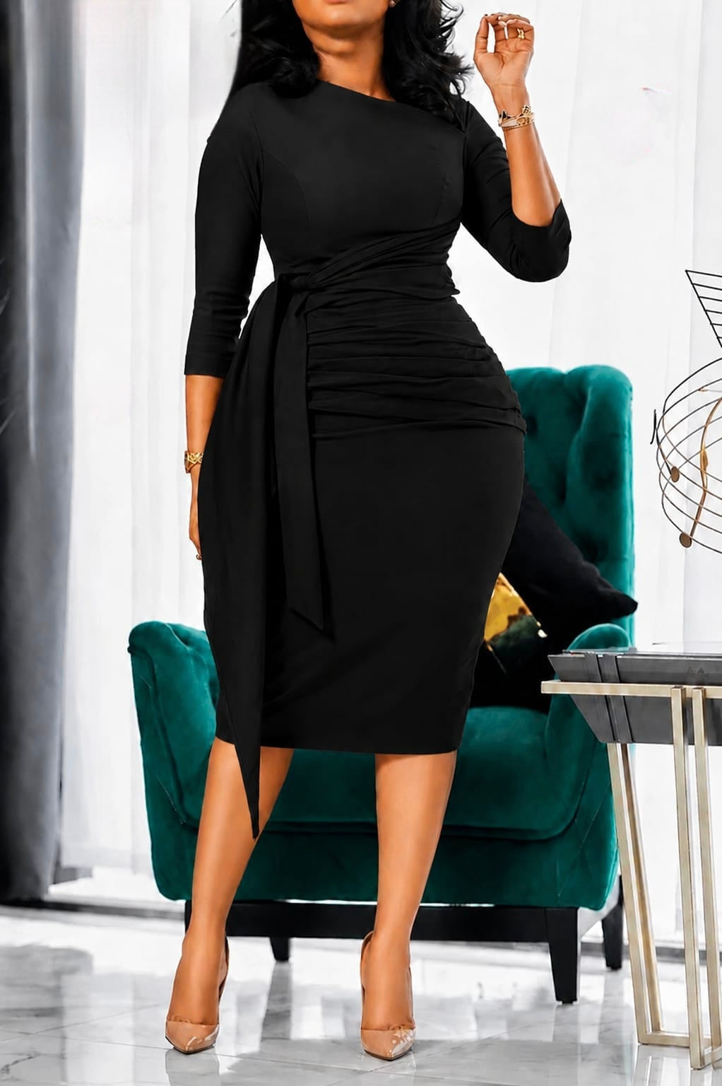 Black Elegant Ruched Waist Midi Dress with three-quarter sleeves and a flowing side sash, model seated on a green chair.