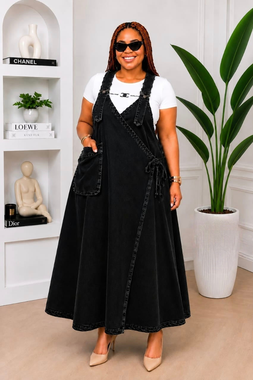 Black denim wrap overall maxi dress with wide adjustable straps, crossover front, and large patch pocket, styled with a fitted white tee.
