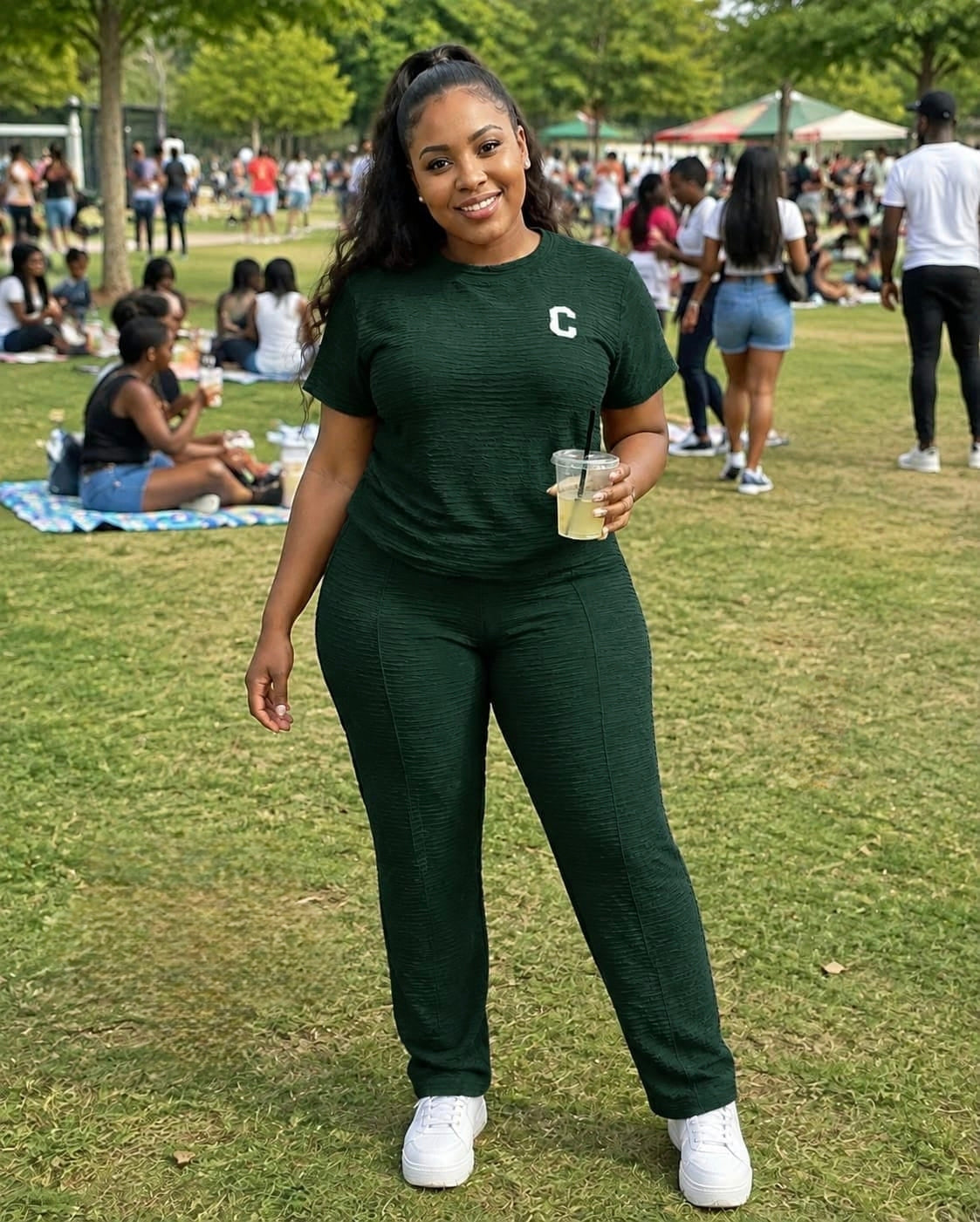Woman in a textured short-sleeve top and straight-leg pants at an outdoor gathering, holding a drink and wearing white sneakers.