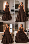 Sleeveless V-neck gown in rich brown with a tiered skirt and ruffle detailing, styled elegantly with a handbag.