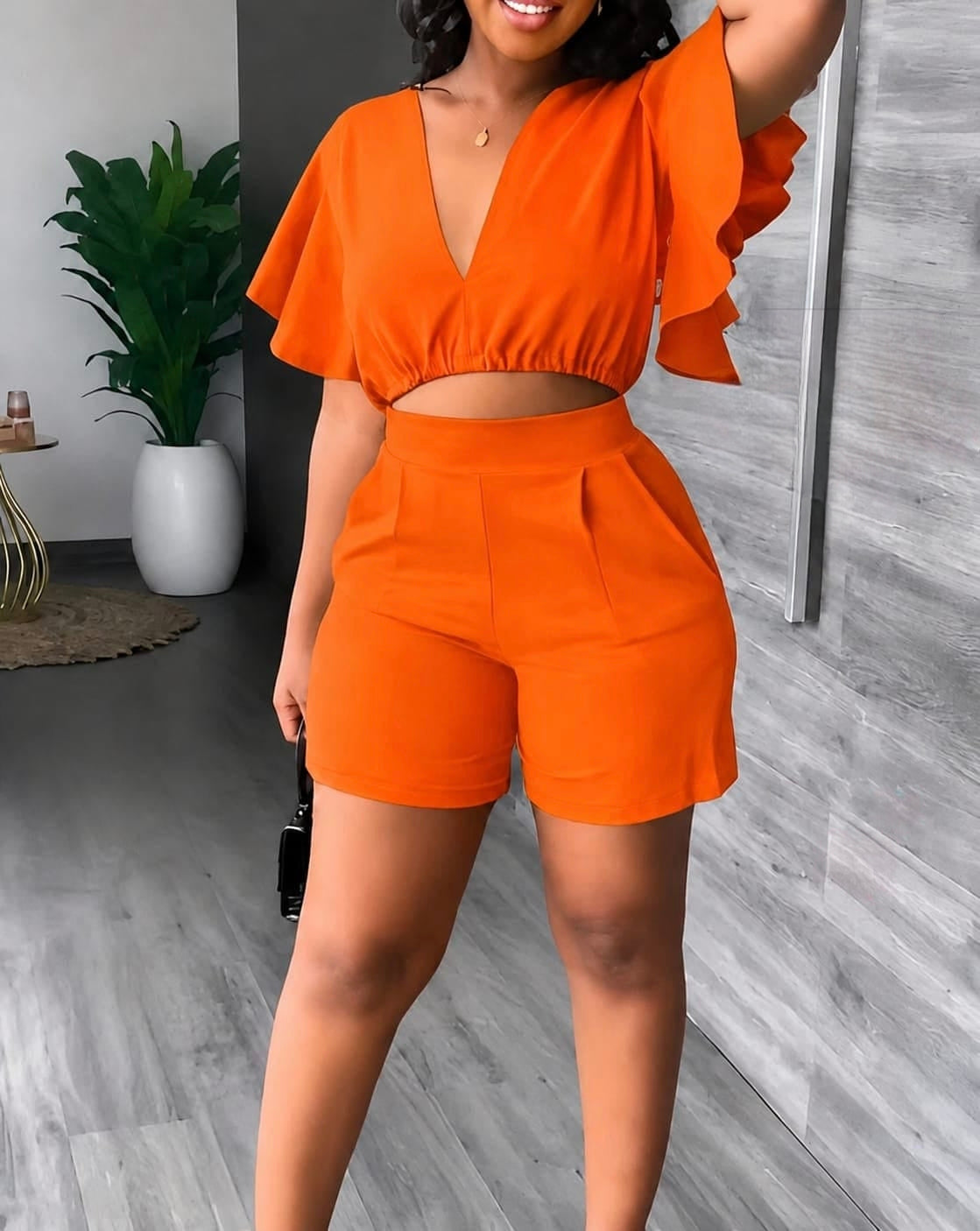 Two-piece orange set featuring a crop top with flutter sleeves and deep V-neckline, paired with high-waisted shorts.