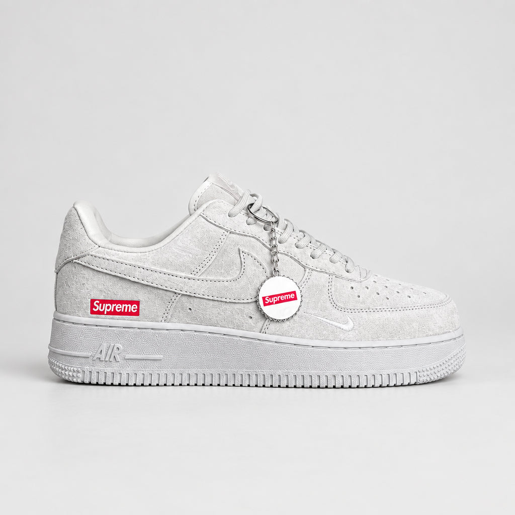 Light grey suede Nike Air Force 1 Low with hot pink and white Supreme box logo and white bottle-cap keychain | Ovadue