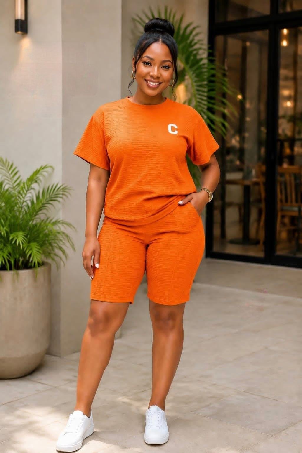 Coordinated orange short-sleeve top and biker-style shorts set with a minimalist chest emblem, styled with white sneakers.