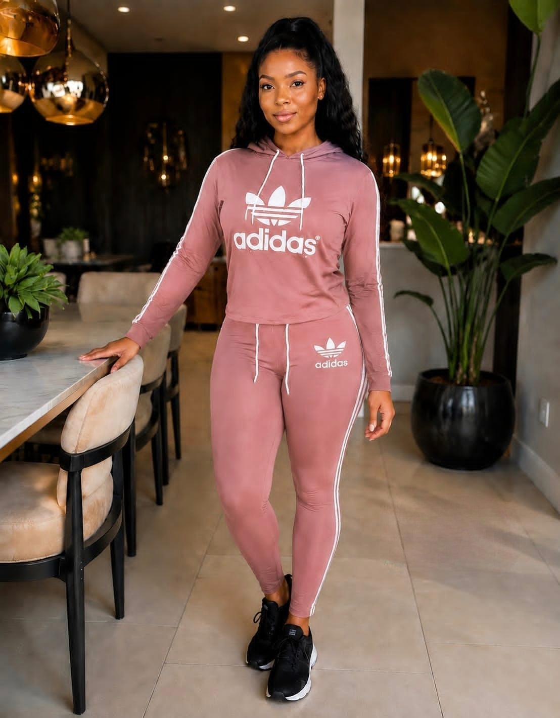 Two-piece pink Adidas tracksuit set featuring a hoodie with drawstring closure and joggers with side stripes.