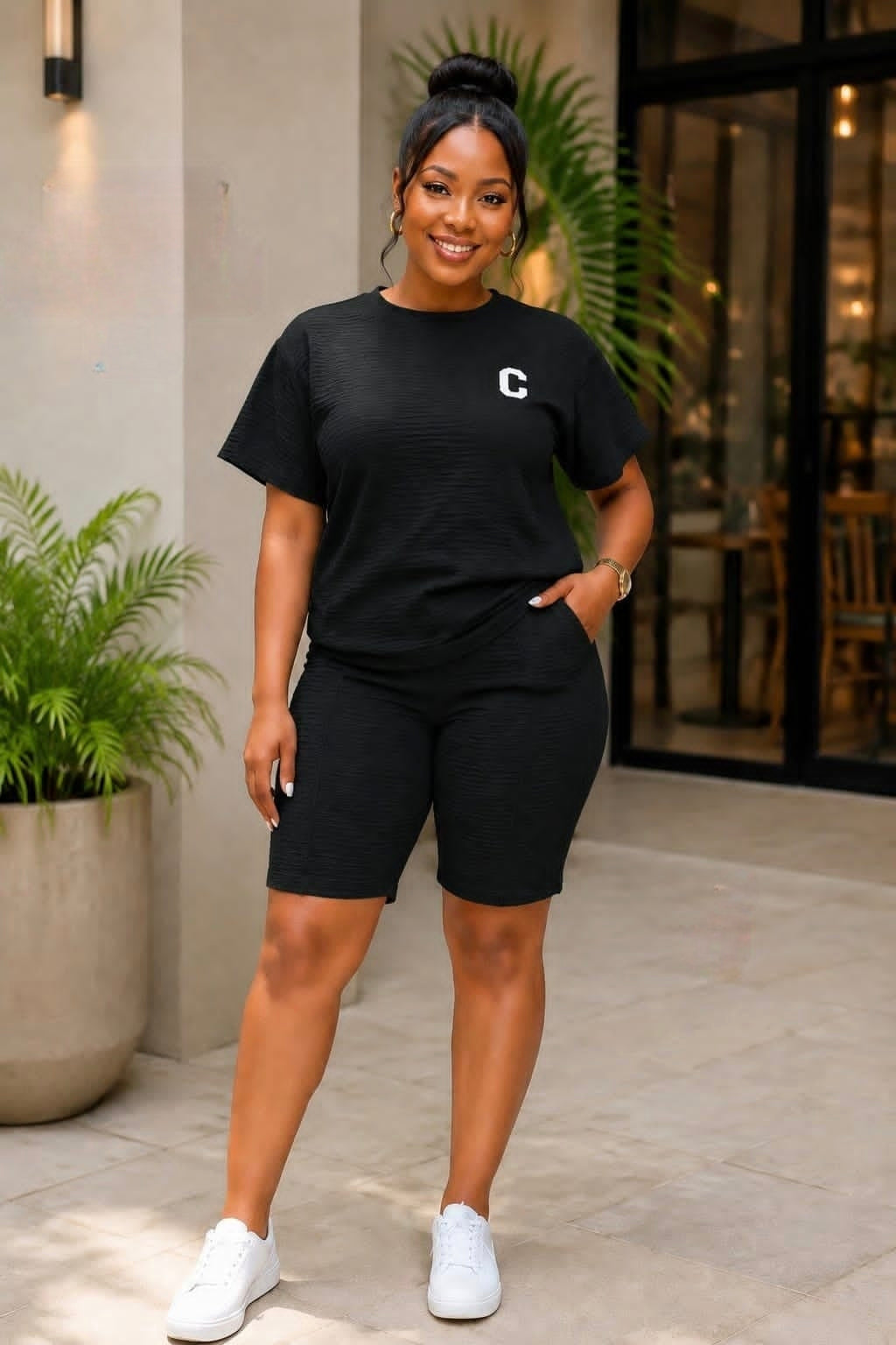 Coordinated black short-sleeve top and biker shorts set with minimalist emblem, styled with white sneakers in a modern setting.