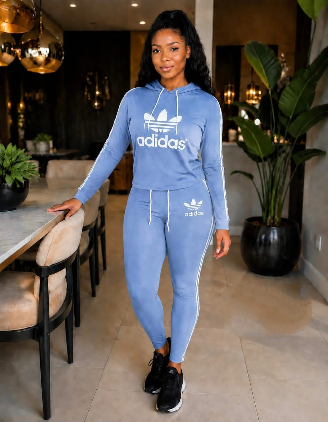 Light blue Adidas tracksuit set featuring a hoodie with drawstring closure and joggers with side stripes. Styled with black sneakers.